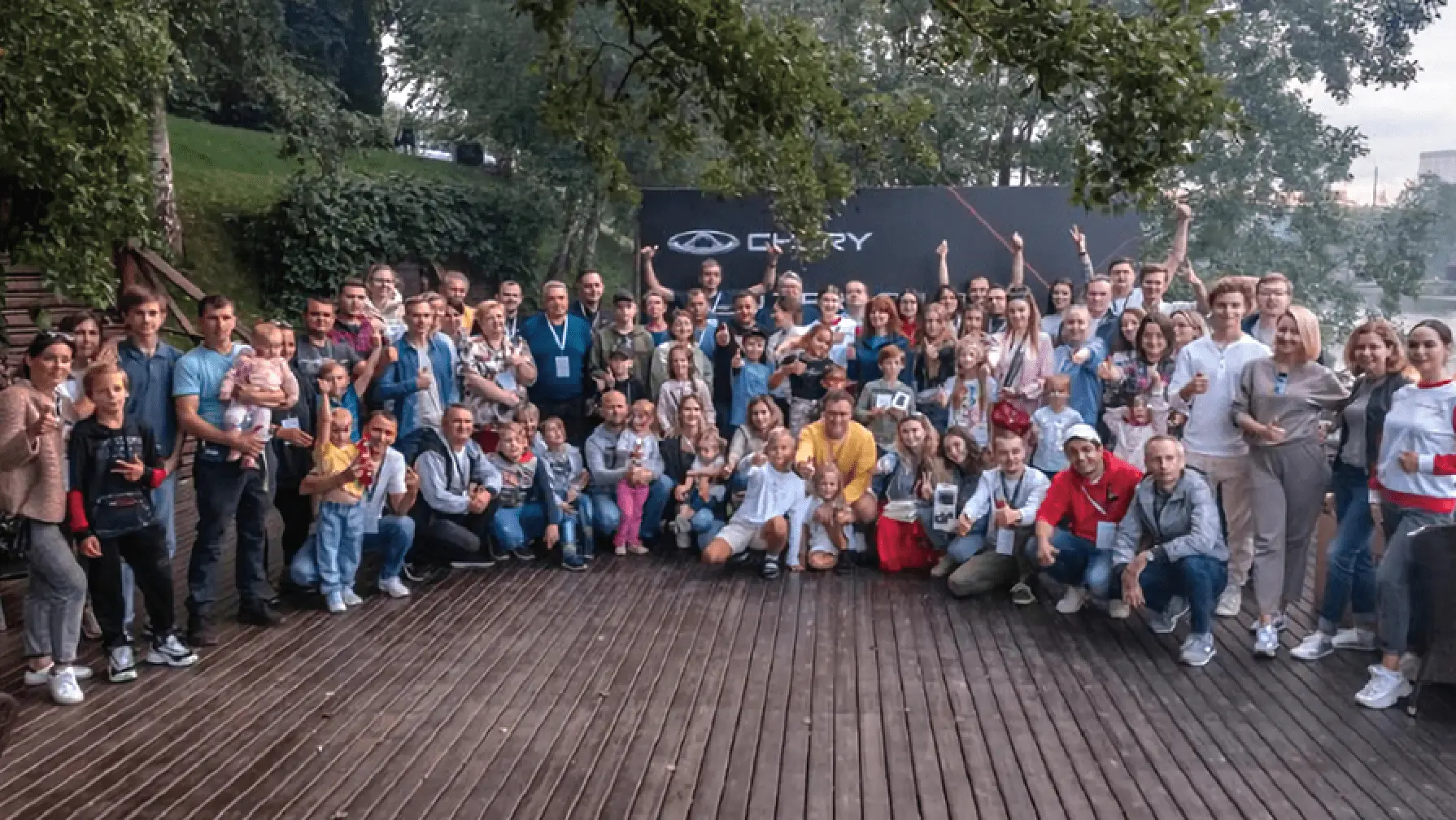 Großes Gruppenfoto der Chery Familie im Freien - Mitarbeiter, Kinder und Familien feiern gemeinsam vor Chery Logo-Banner